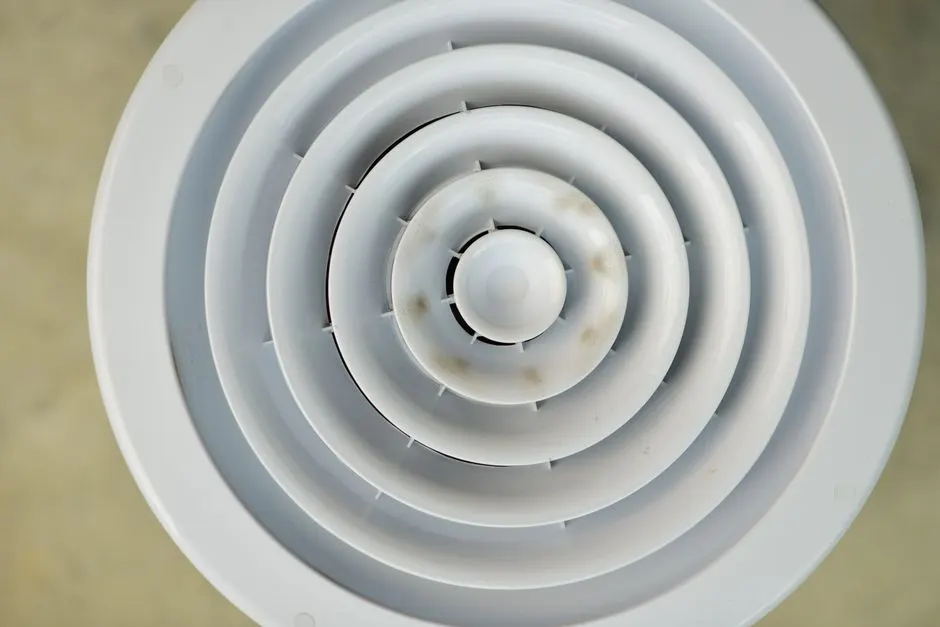 Top view of a white circular air vent highlighting its concentric design with slight discoloration.